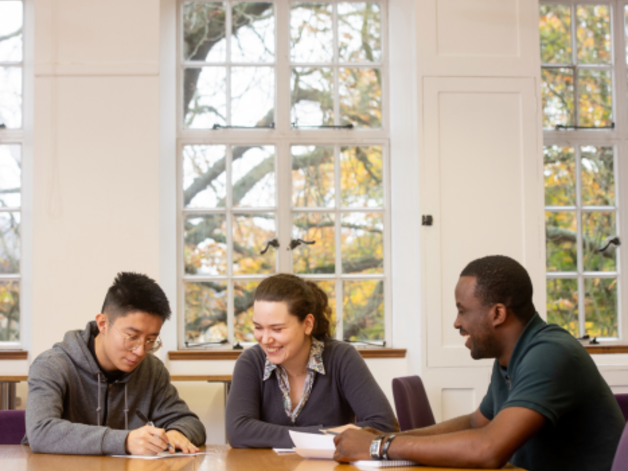 Three postgrads sit in a seminar in our reading room at oathology, laughing and smiling 